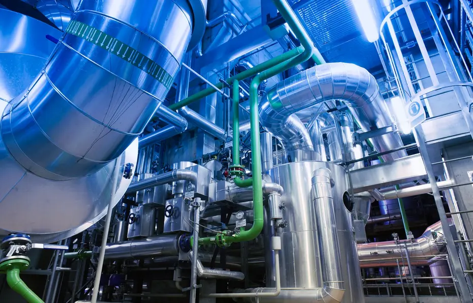 Blick in eine Industrieanlage mit verzweigten, isolierten Edelstahlrohrleitungen in blauem Licht
