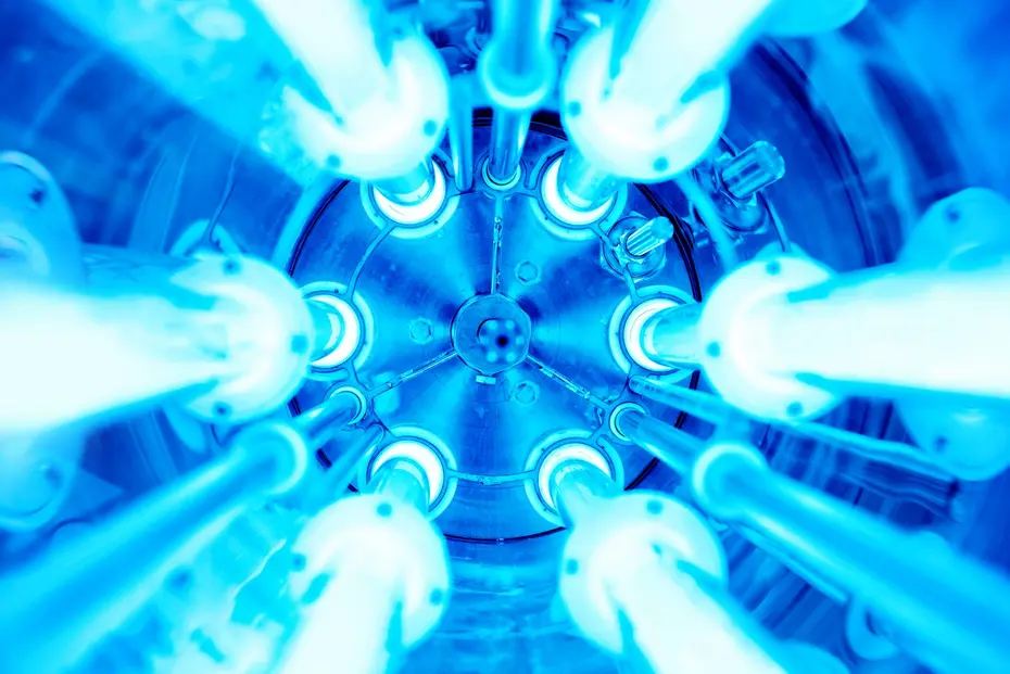Acht kreisförmig angeordnete, blau leuchtende UV-Lampen im Inneren eines zylindrischen Reaktors, Blick von unten